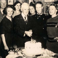 Cousins Dorie and Clara are identified as the younger women in the front row. Presumably, their father is cutting the cake.